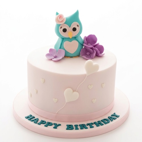 Round pastel pink birthday cake with a blue fondant owl, purple flowers, and white hearts.