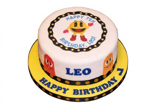 Round white Pacman themed birthday cake with ghost characters, black dotted border, and custom age.