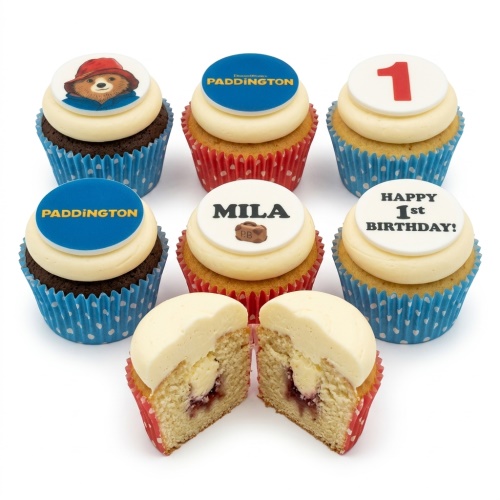 Set of Paddington Bear themed birthday cupcakes with blue and red cases, featuring character and logo toppers, and one cupcake cut in half.