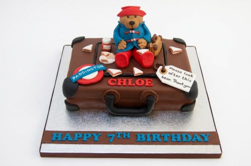 Paddington Bear cake shaped like a brown suitcase with marmalade sandwiches, a Paddington sign, and a custom name and age.