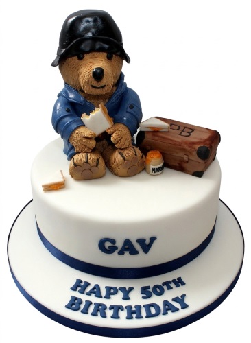 White round cake with 3D Paddington Bear figure, suitcase, and marmalade jar.