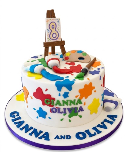 White round cake with colourful paint splatters, topped with an easel, paint tubes, palette, and brush, with custom age topper.
