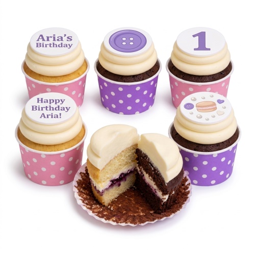 Six cupcakes with white frosting, pink and purple polka dot wrappers, and custom birthday toppers including a number 1, button, macaron, and personalised messages.