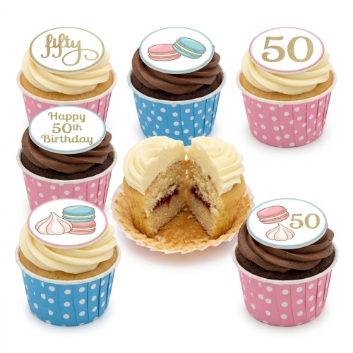 Assortment of elegant birthday cupcakes with macaron and meringue toppers in pink and blue polka dot cases.