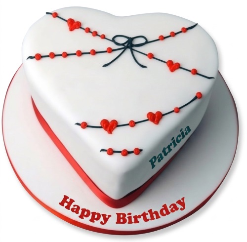 White heart shaped cake with red hearts, red beads, black bow, and red ribbon.