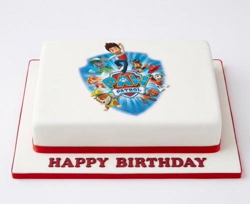 Square white Paw Patrol birthday cake with red ribbon and "Happy Birthday" message.