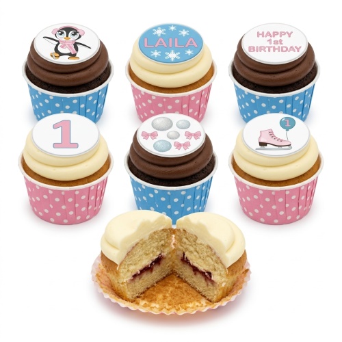 Selection of 1st birthday cupcakes for girls with penguin, ice skate, and snowflake toppers, in pink and blue wrappers.