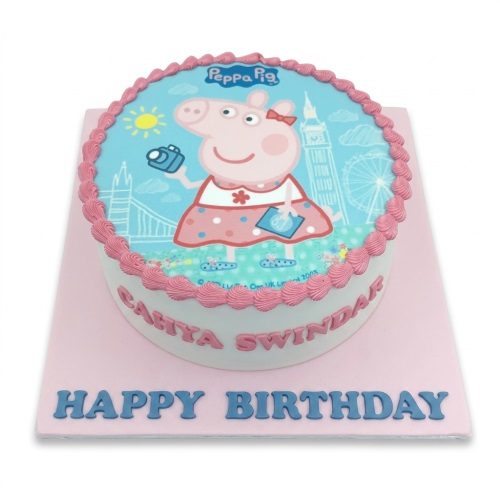 Round white cake with pink piping and an edible image of Peppa Pig in London, with a custom name and 'Happy Birthday' message.