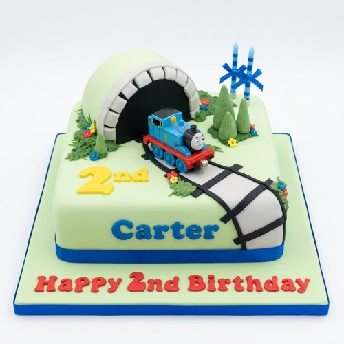 Light green square Thomas The Tank Engine birthday cake with tunnel, tracks, trees, and custom age candles.