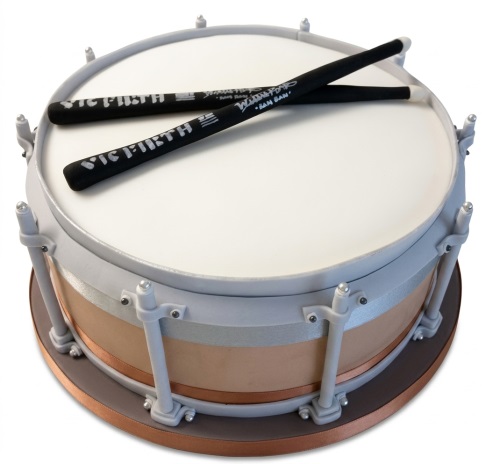Round cake decorated to look like a white and copper snare drum with two black drumsticks on top.