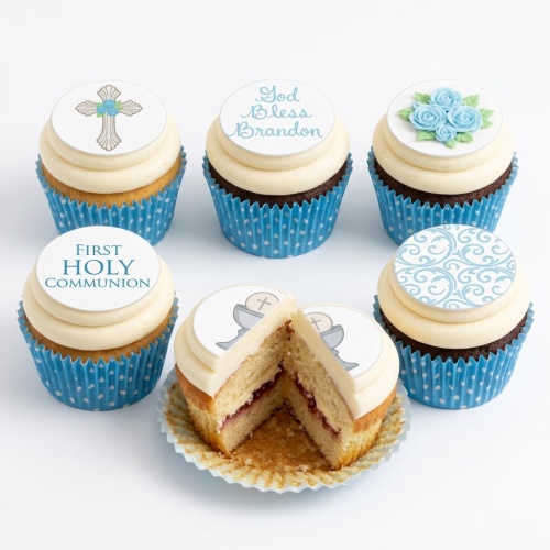 Vanilla and chocolate cupcakes with white frosting, blue polka dot cases, and edible religious celebration toppers featuring a cross, chalice, blue roses, and 'First Holy Communion' message.