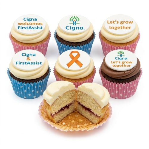 Six corporate cupcakes with white frosting and custom edible toppers featuring company logos and messages, one cut open to show vanilla sponge and jam filling.