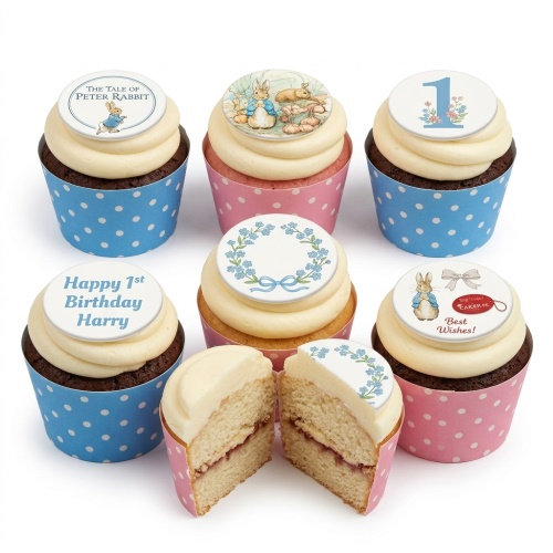 Set of Peter Rabbit themed cupcakes with white buttercream and edible toppers, some with Peter Rabbit illustrations, a number 1, a floral wreath, and custom messages.