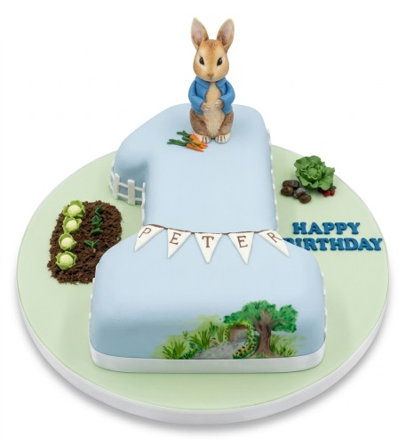 Light blue number 1 cake with Peter Rabbit figurine, garden, and 'Happy Birthday' message.