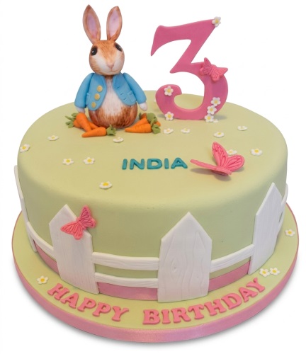 Round light green Peter Rabbit birthday cake with a pink custom age topper, personalised name, and white picket fence.
