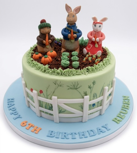 Peter Rabbit themed birthday cake with rabbit figures, garden decorations, and a custom age topper.