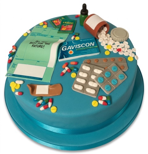 Round blue cake with edible medical decorations including pills, bottles, blister packs, and a prescription pad with a custom message.