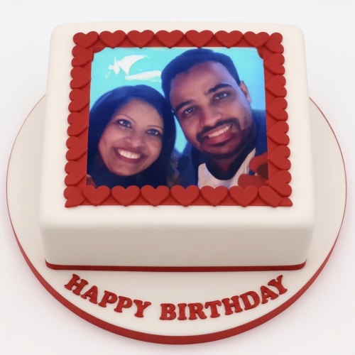 White square birthday cake with a custom photo framed by red hearts and a 'Happy Birthday' message.