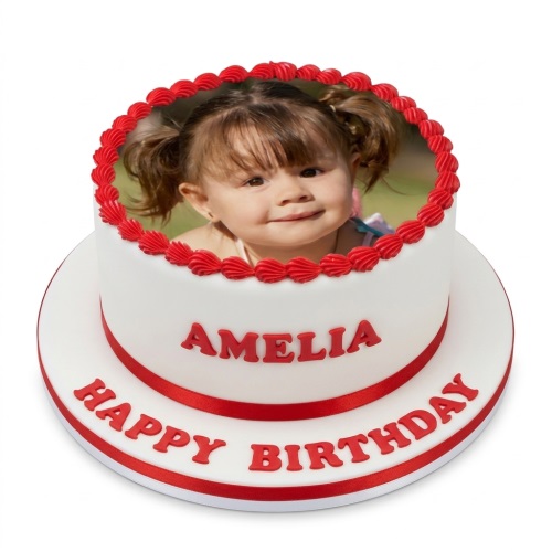 Round white two-tier cake with an edible photo of a child on top, red piped border, red ribbon, and red 'Happy Birthday' message.