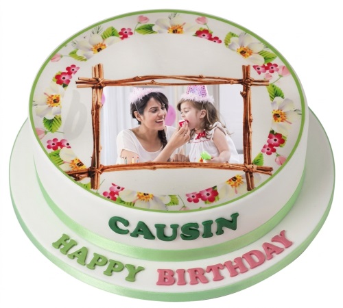 Round two-tiered white cake with an edible photo print, rustic frame, and floral border, with green and pink lettering.