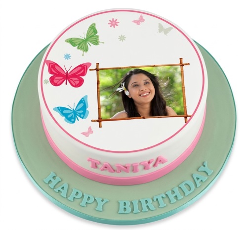 Round white birthday cake with green, pink, and blue butterflies, a custom photo in a bamboo frame, and a personalised name and message.