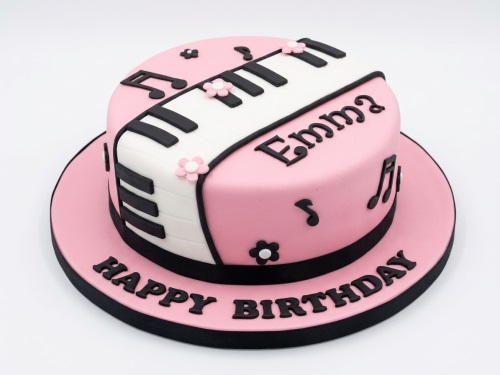 Pink round birthday cake with white and black piano keyboard design, musical notes, and small flowers.