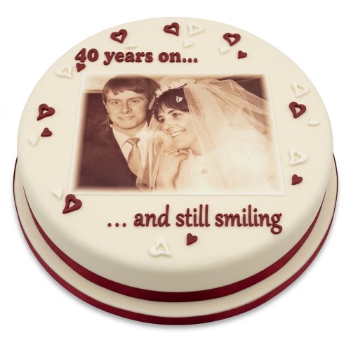 Round 40th anniversary cake with an edible photo of a couple and red heart decorations.
