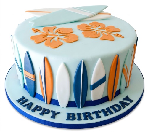 Round light blue fondant cake decorated with orange hibiscus flowers and multiple colourful surfboards around the sides and on top, with 'Happy Birthday' written at the base.