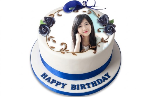White round birthday cake with personalised photo, blue roses, green leaves, brown vines, and 'Happy Birthday' message.