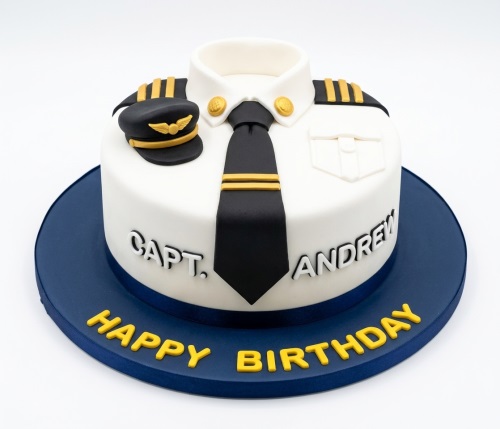 Round white cake decorated as a pilot's uniform with black tie, gold epaulets, and hat. Personalised with a name and 'Happy Birthday'.