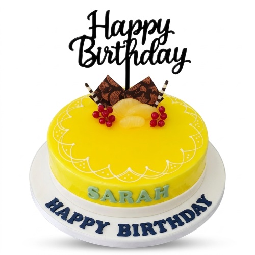 Round yellow glazed birthday cake with "Happy Birthday" topper, red berries, orange fruit, chocolate decorations, and a custom name.