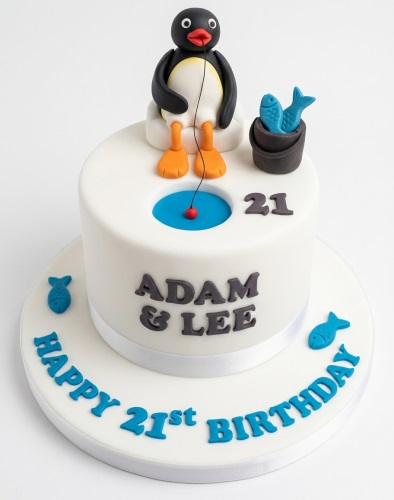 White fondant birthday cake with Pingu figurine fishing, blue water, fish bucket, and custom age.