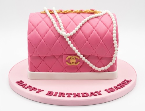 Pink quilted handbag shaped cake with gold chain, pearl necklace, and gold logo on a pink cake board.