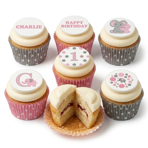 Six vanilla cupcakes with white frosting, pink and grey polka dot wrappers, and edible elephant-themed toppers for a 1st birthday.