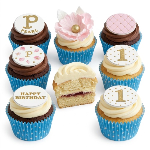 Assortment of floral and personalised birthday cupcakes with pink, gold, and white toppers in blue polka dot wrappers.