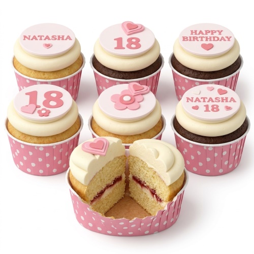Pink birthday cupcakes with cream frosting, decorated with hearts, flowers, and custom age/name toppers in pink polka dot wrappers.