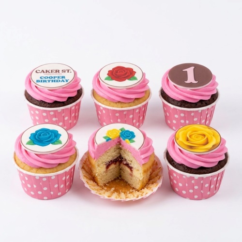Set of six floral birthday cupcakes with pink buttercream and edible rose toppers, one with a custom age '1' and another with 'COOPER BIRTHDAY'.