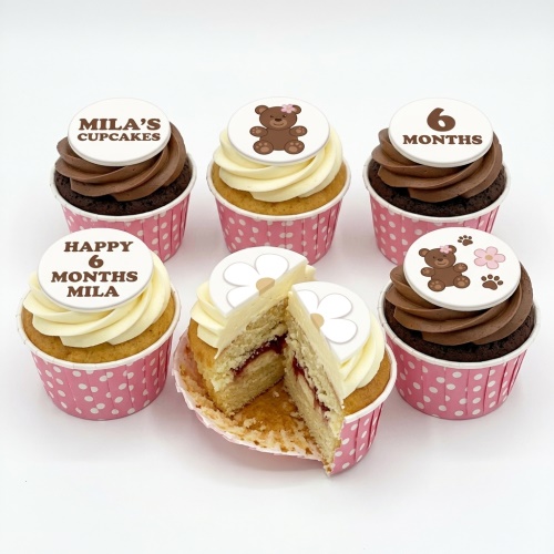 Assortment of baby celebration cupcakes with teddy bear and flower toppers, featuring custom age and name examples.