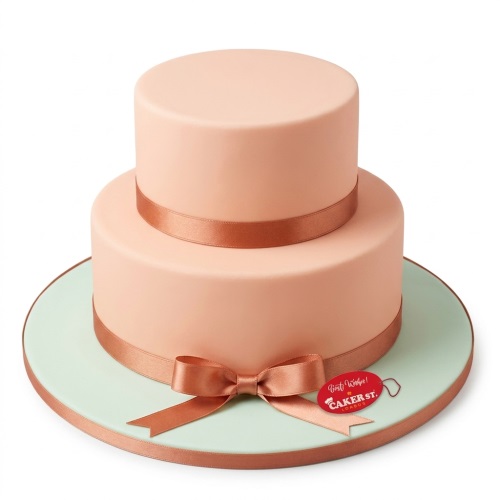 Two tier peach cake with copper ribbon and bow on a mint green board.