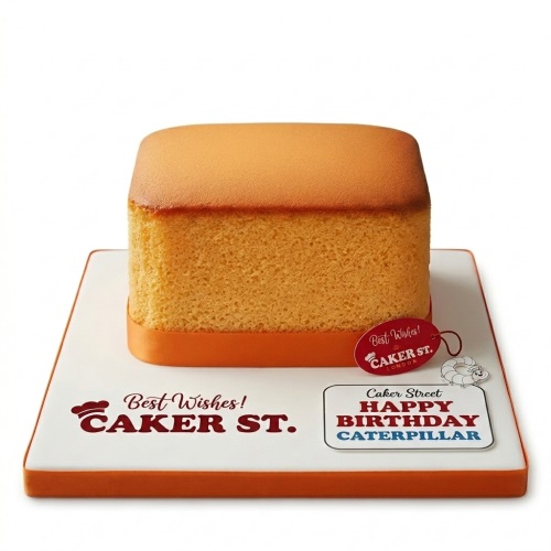 Rectangular orange sponge cake with a white board, "Happy Birthday Caterpillar" plaque, and small caterpillar figure.