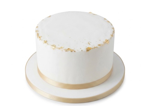 White single-tier birthday cake with gold leaf accents and a gold ribbon.