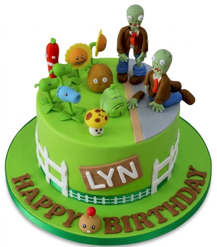 Round green Plants Vs Zombies themed birthday cake with edible zombie and plant characters, a white picket fence, and a personalised name plaque.