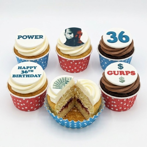 Six cupcakes with white and chocolate frosting, some with Power TV show and money themed toppers, in red and blue polka dot cases. One cupcake is cut open revealing jam filling.