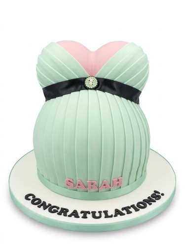 3D sculpted cake shaped like a mint green pleated maternity dress with pink top and black ribbon.