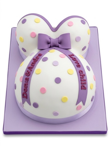 White pregnant belly cake with purple bow and colourful polka dots on a purple board.