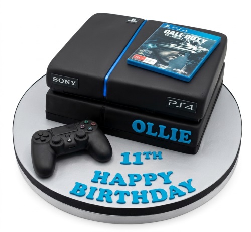 Black PlayStation console cake with controller and game on a silver board.