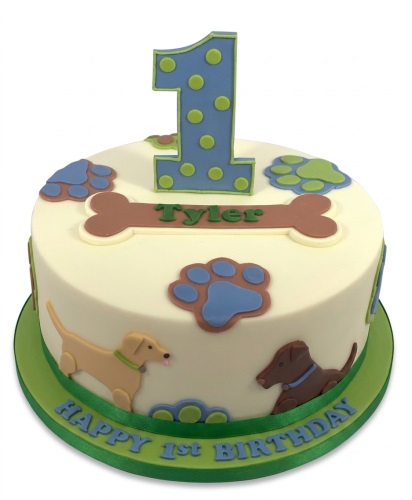 Round 1st birthday cake with blue polka dot number one, dog figures, paw prints, and a bone with a personalised name.