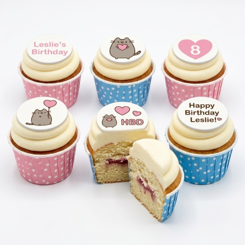 Set of Pusheen cat themed birthday cupcakes with white frosting, pink and blue polka dot cases, and custom age/message toppers.