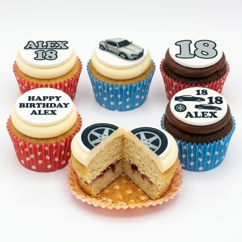 Assortment of car-themed birthday cupcakes with custom age and name toppers in red and blue wrappers.
