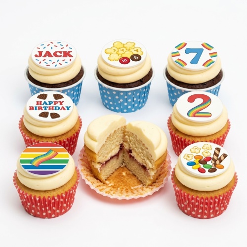 Assortment of colourful birthday cupcakes with various toppers including numbers, a name, happy birthday message, rainbow, popcorn, and candy.